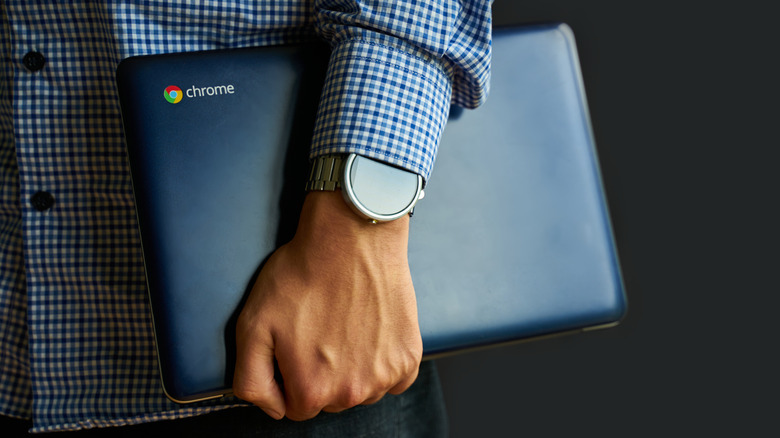 A man holding a Chromebook with a blue-checkered shirt