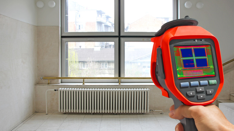A person using a thermal camera on a windows and a radiator.