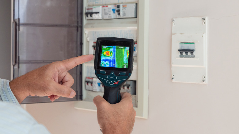 A person checking the fuse box with a thermal camera.