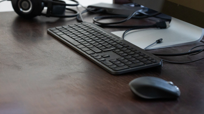 A black keyboard and mouse sit on a wooden desk.