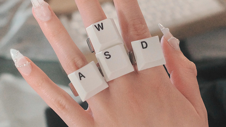 A close up photo of a hand wearing four rings, each with a key cap as the accent.