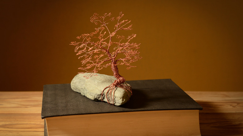 Copper wire art of a tree coiled around a rock on top of a book.