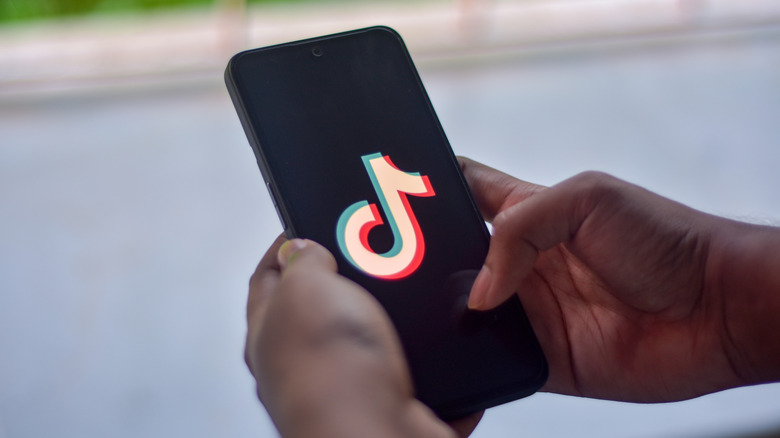 A man holding a phone with a TikTok logo on display