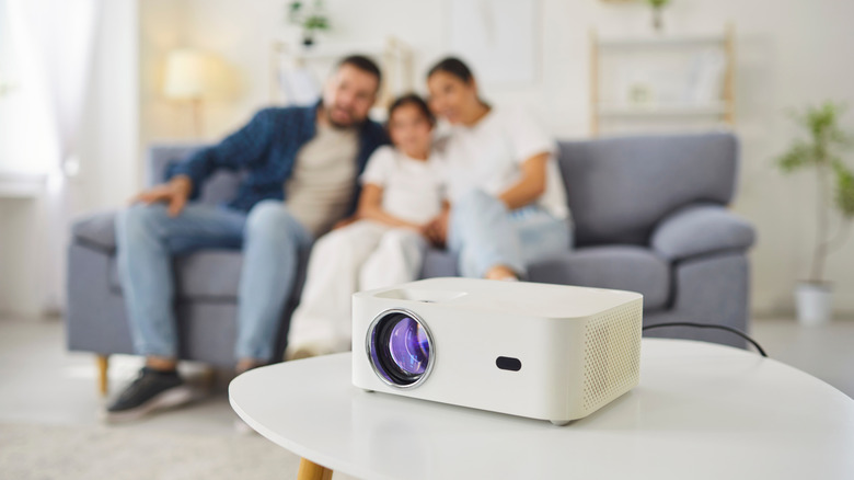 Family sitting in living room blurred in the background with focus on a white projector in the foreground