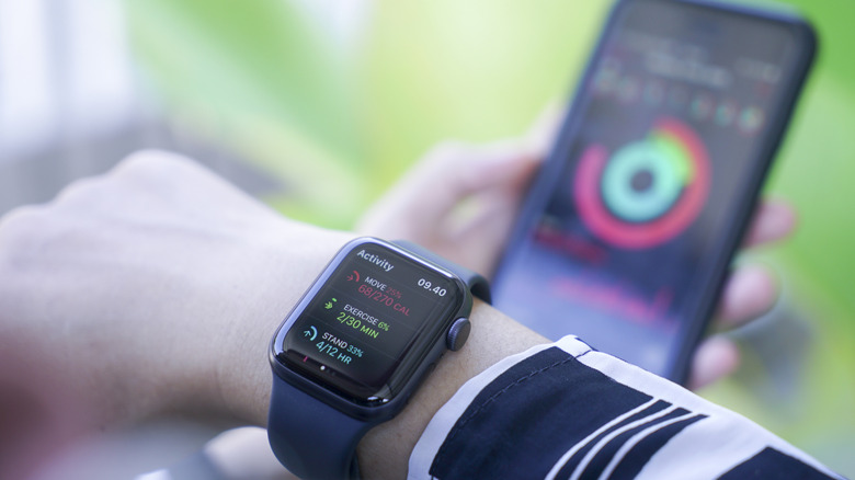 A person with an Apple Watch on their wrist and an iPhone in the background.