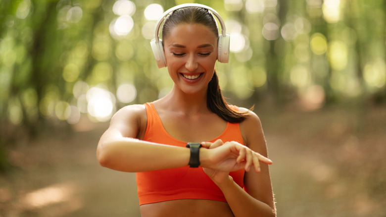 A happy woman in workout wear outdoors, looking at her smartwatch.