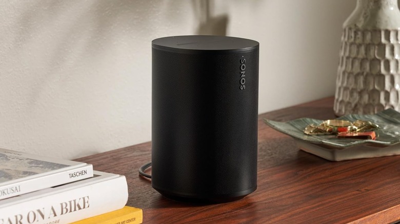 The Sonos Era 100 smart speaker on a wooden surface.