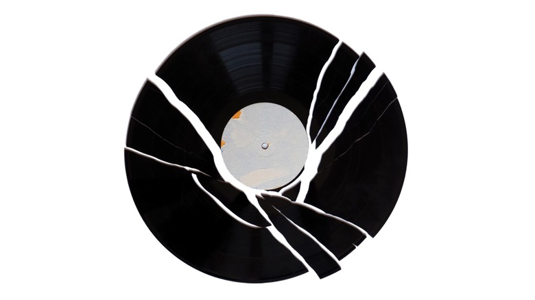 Broken vinyl record with multiple cracks and missing pieces, photographed from above against a plain white background.