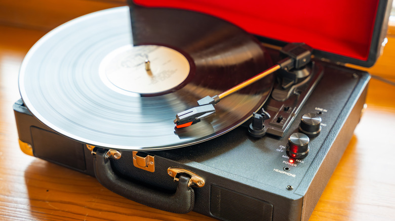 Portable suitcase-style record player playing a vinyl record, with the turntable platter spinning and the tonearm positioned on the record.