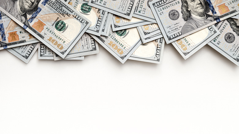 Pile of U.S. $100 bills scattered across a white background, with empty space below for text or graphic design.