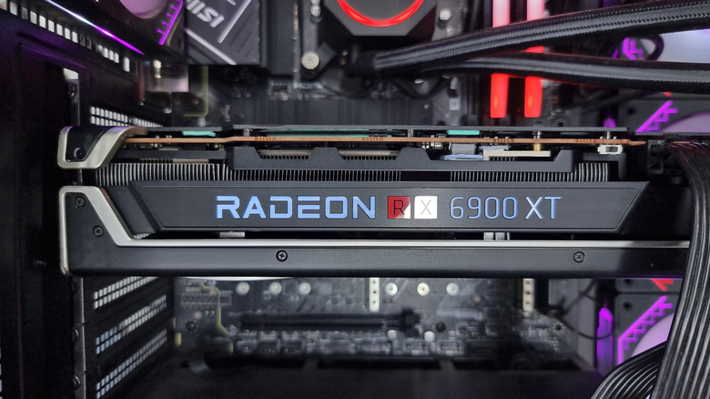 Close-up of an AMD Radeon RX 6900 XT graphics card installed inside a desktop gaming PC, with RGB-lit components and liquid cooling visible in the background.