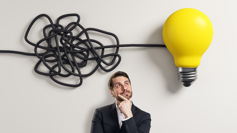 A man in a suit thinking, tangled wires leading to a lightbulb over his head