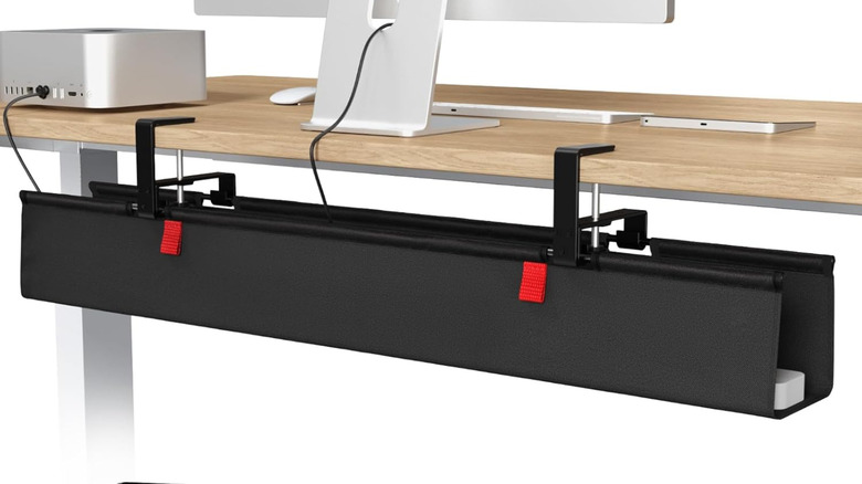 A fabric computer cable management tray is clamped onto the back of a desk, hiding various cables