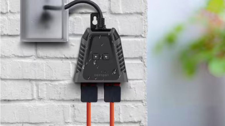 Defiant outdoor smart plug in black against white brick