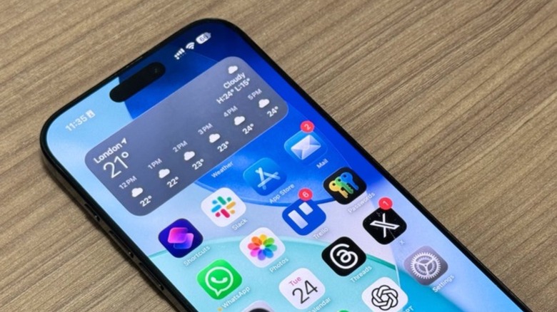 An iPhone on a table. On the display, some apps on the Home Screen and a weather widget.