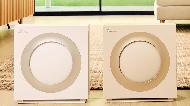 Two Coway Airmega Mighy 2 air purifiers stand next to each other in a living room. One white, and one beige.