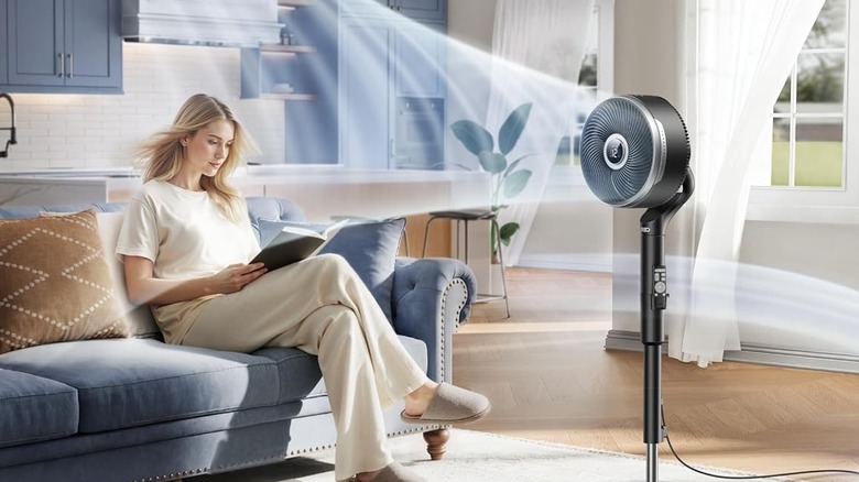 A woman has a vortex of air blown at her by a large standing fan.