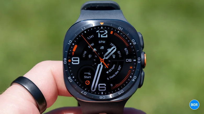 A person holds a Samsung smartwatch so that the screen showing a clockface is clearly visible.