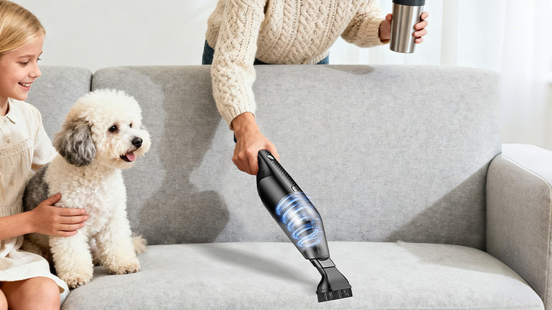 A woman using the Antaha Cordless Handheld Vacuum Cleaner on a couch while a girl and a dog are sitting on it.