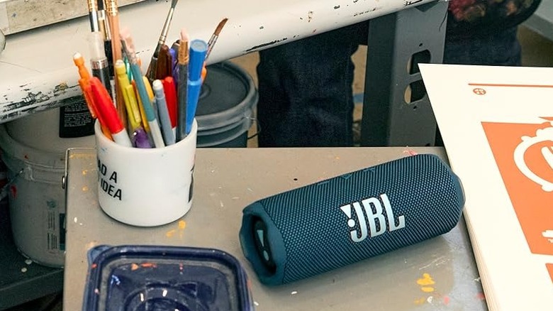 The JBL Flip 7 Portable Speaker on a desk, surrounded by work clutter.