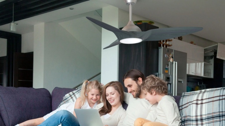 The Atomi Smart Monarc 52" Wi-Fi Indoor Ceiling Fan installed in the living room, over a family sitting on a couch.