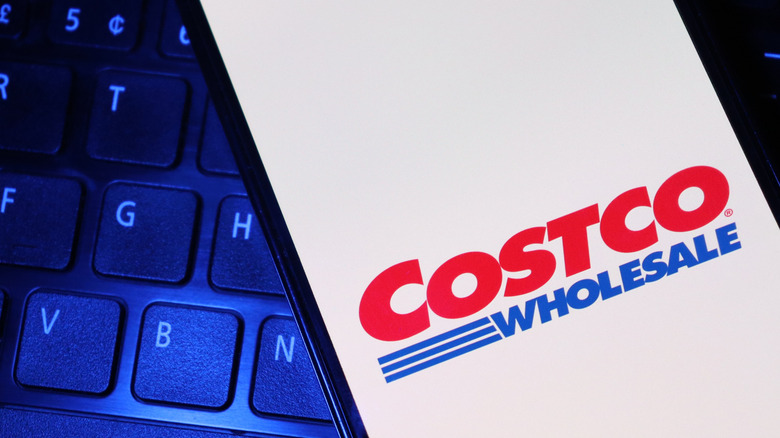 A smartphone with the Costco logo on the screen, on top of a keyboard.