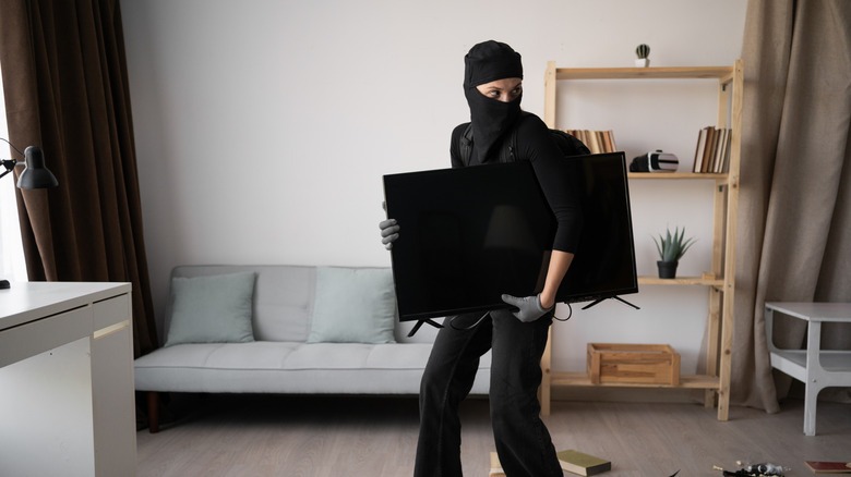 A burglar dressed in black stealing a TV from a house