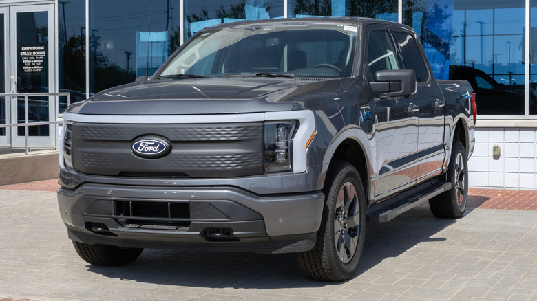 A dark gray Ford F1-150 Lightning parked in front of a dealership.