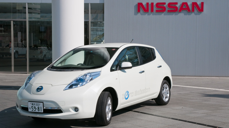 A white Nissan Leaf parked in front of a Nissan dealership.
