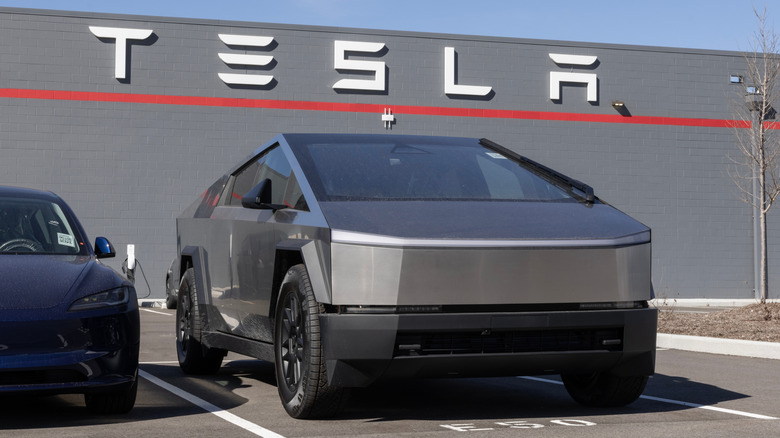 A silver Tesla Cybertruck parked in front of a gray building with a large Tesla logo on it.