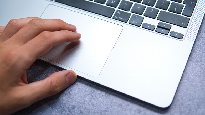 A person's fingers rest on a silver MacBook trackpad.