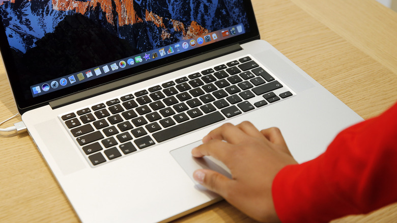A right hand hand operates a MacBook trackpad with multiple fingers at once.