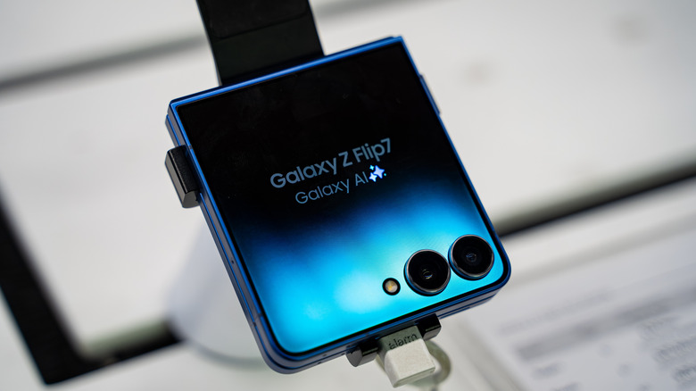 A Galaxy Flip phone sits on a display stand with its cover screen visible.