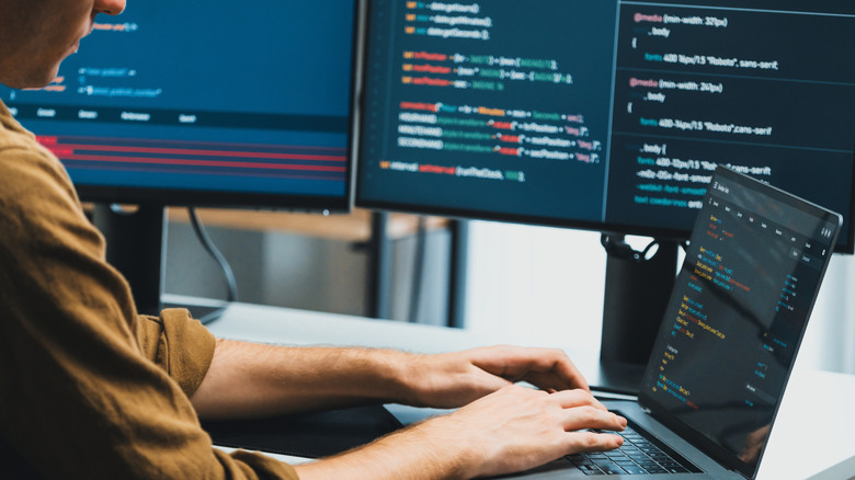 A person typing code using multiple screens