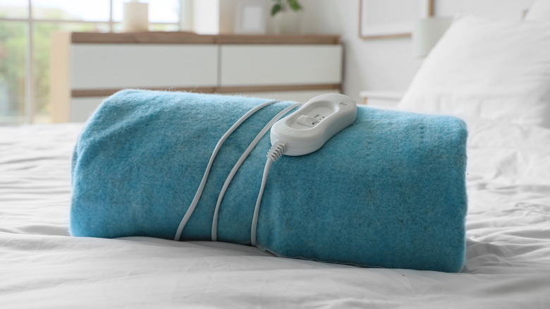 Electric heated blanket with an integrated temperature controller rolled up on a bed.