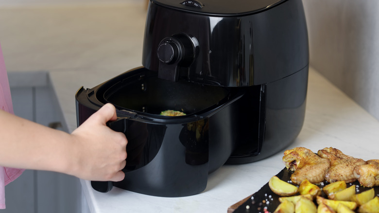 Person removing the cooking basket from an air fryer after preparing food.