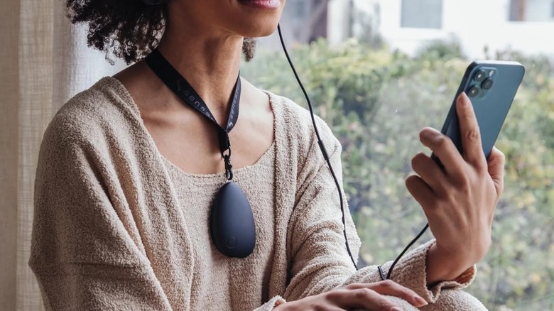 A person wearing the Sensate Relaxation Device using a lanyard while looking at their phone