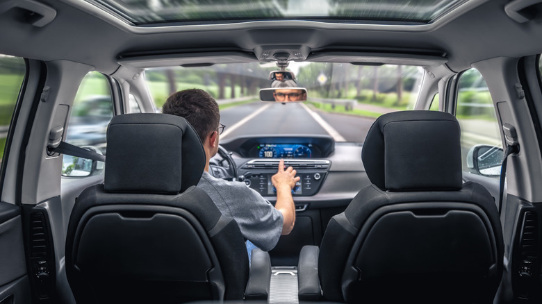 A person behind the wheel of a vehicle, while using technology on the dashboard.