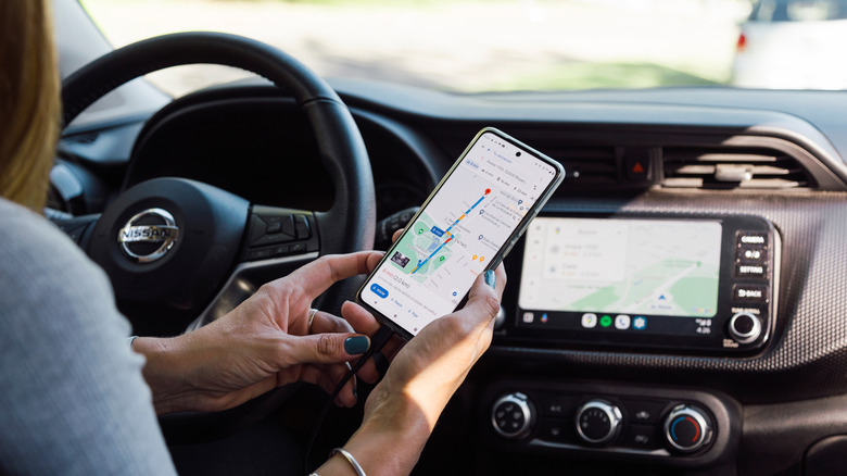 A woman holding a smartphone with Google Maps open while sitting in a car.