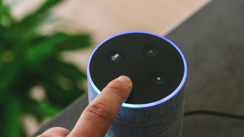 A finger pressing a button on top of an Amazon Echo speaker.