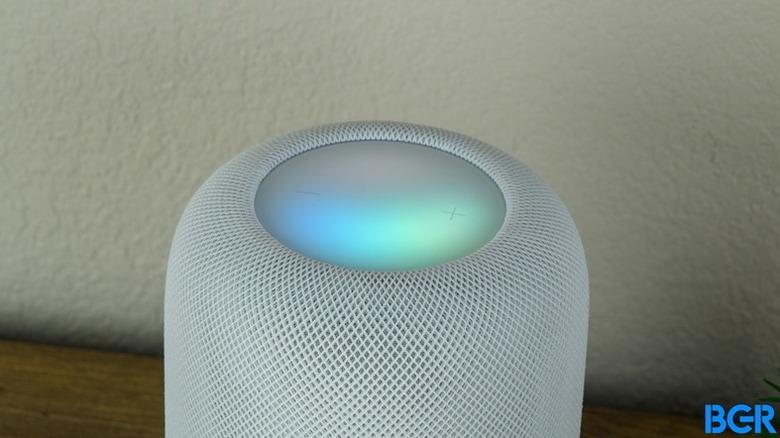 The second generation Apple HomePod sitting on top of a table in front of a white wall.