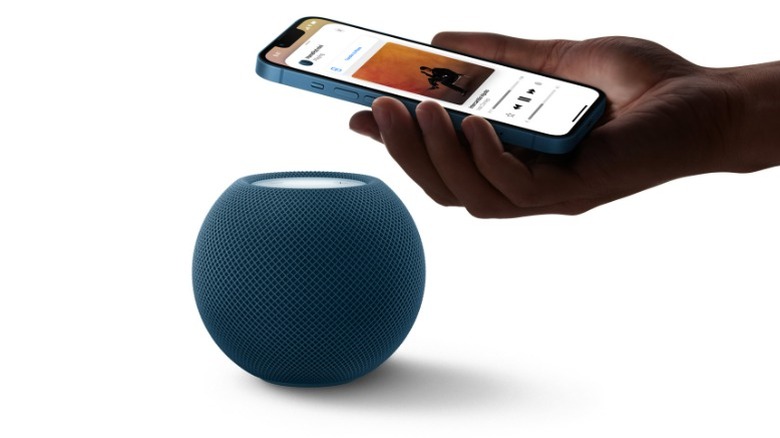 A person holding an iPhone playing music over the HomePod Mini smart speaker