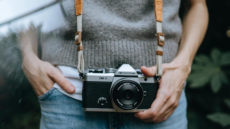 The OM System OM-3 mirrorless camera with its strap hanging around a person's neck.