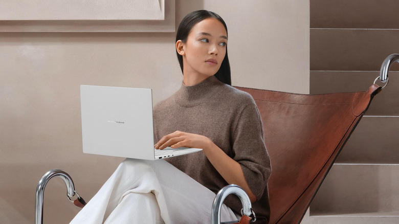 A woman sits in a modern leather chair holding an open laptop on her knee.