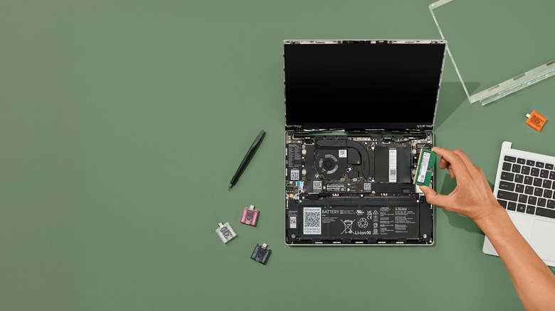 A laptop computer lies open on a green surface with its back cover removed, exposing internal components.