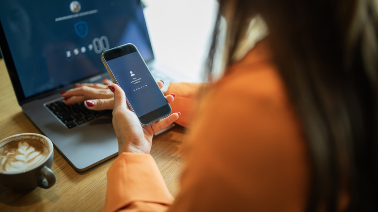 Woman using her smartphone to input a password onto her laptop