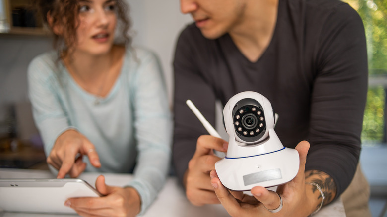 A man holding a security camera and a woman holding a tablet.