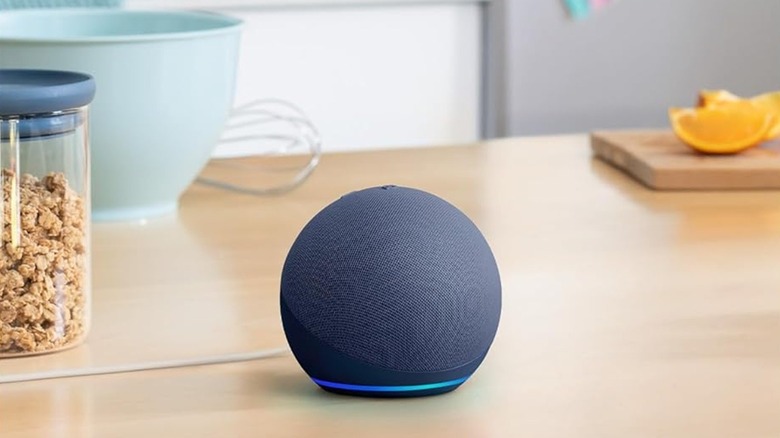 The Amazon Echo Dot (5th Gen) smart speaker on a kitchen table, with some ingredients and utensils behind it.
