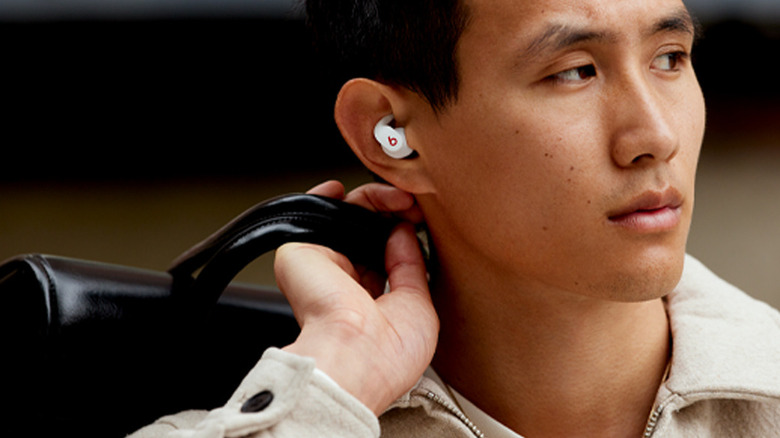 A mean wears a set of Beats Fit Pro buds, looking off-camera with a briefcase slung over his shoulder.