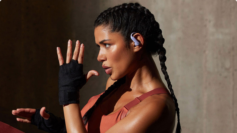 A woman looking off camera with a gloved hand raised while wearing Beats Powerbeats Pro 2 buds.